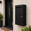 Matte black large parcel letter box mounted on a cream brick residential entrance wall with front letter slot and secure key lock